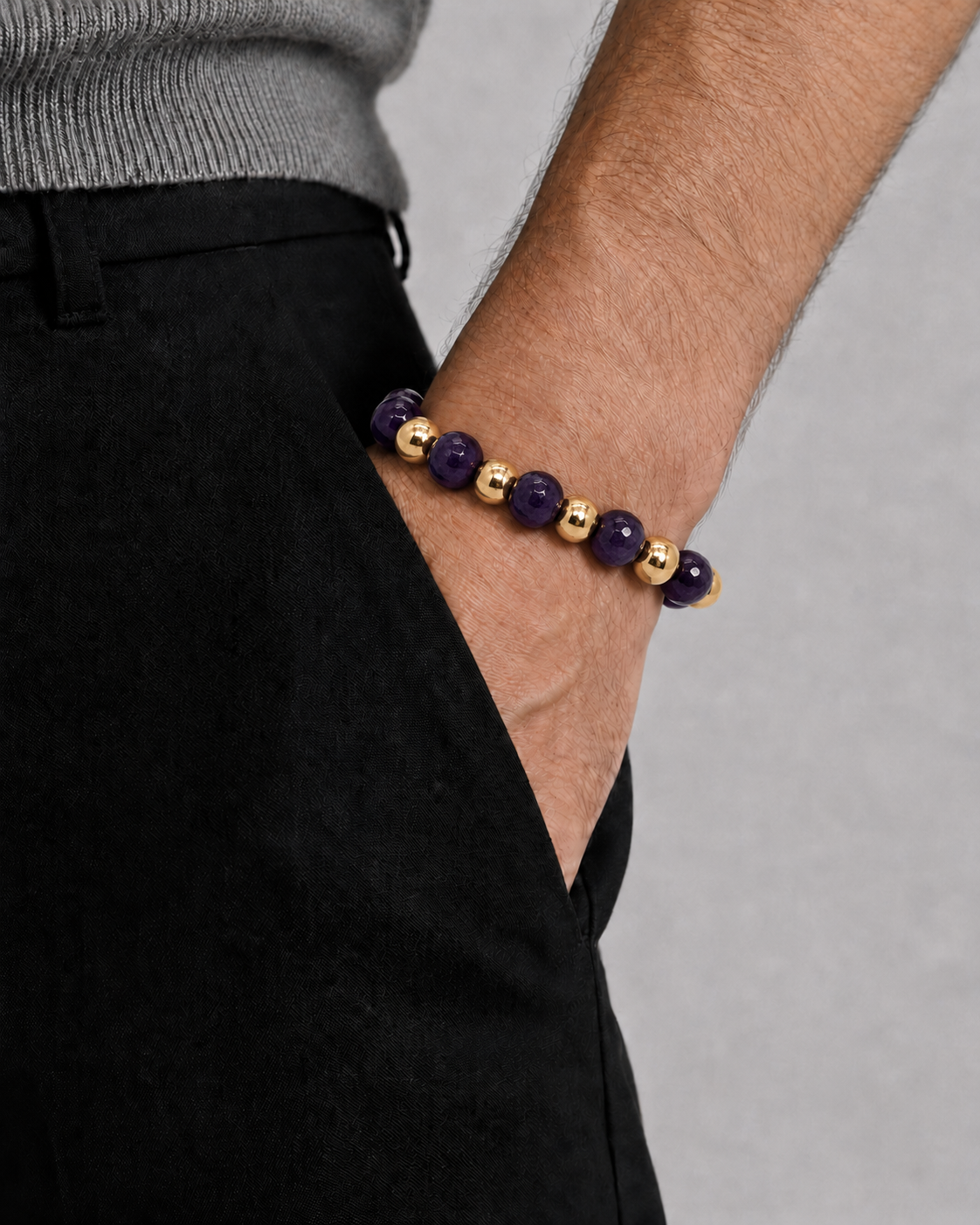 Bracelet with purple and gold beads on a wrist against a gray background