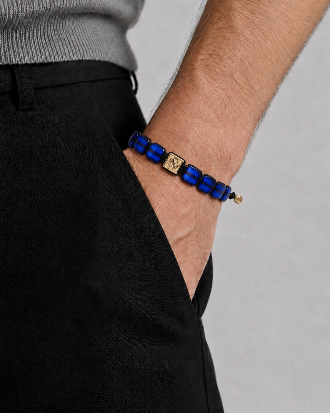 Person wearing a blue beaded bracelet with a gold clasp on a plain background