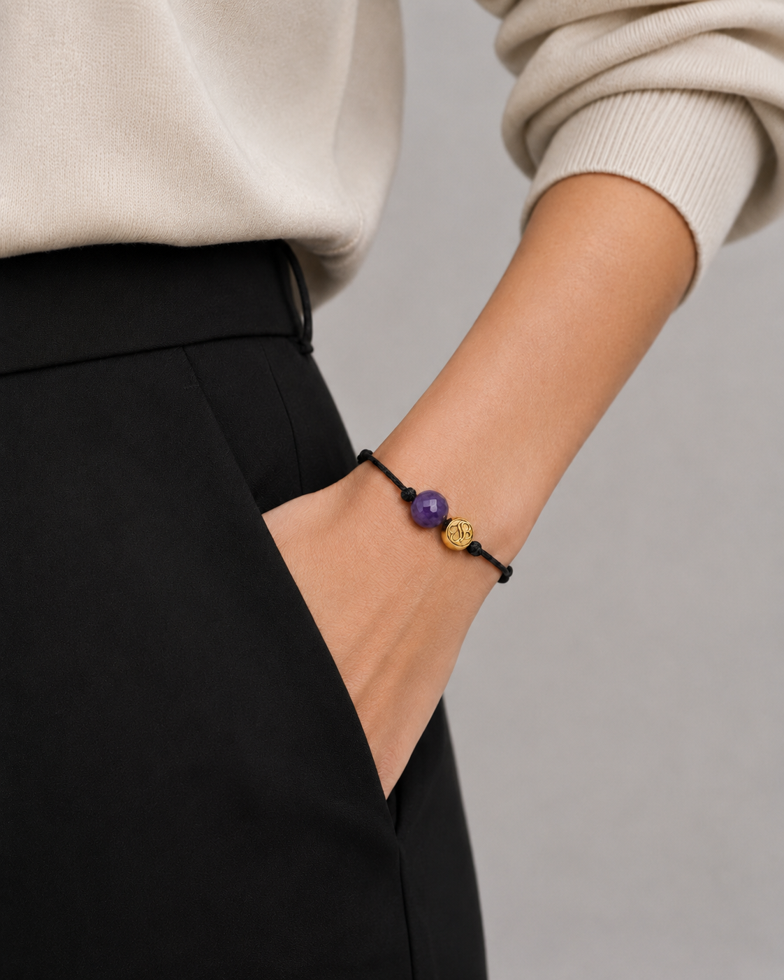 Person wearing a bracelet with purple and gold beads on a neutral background