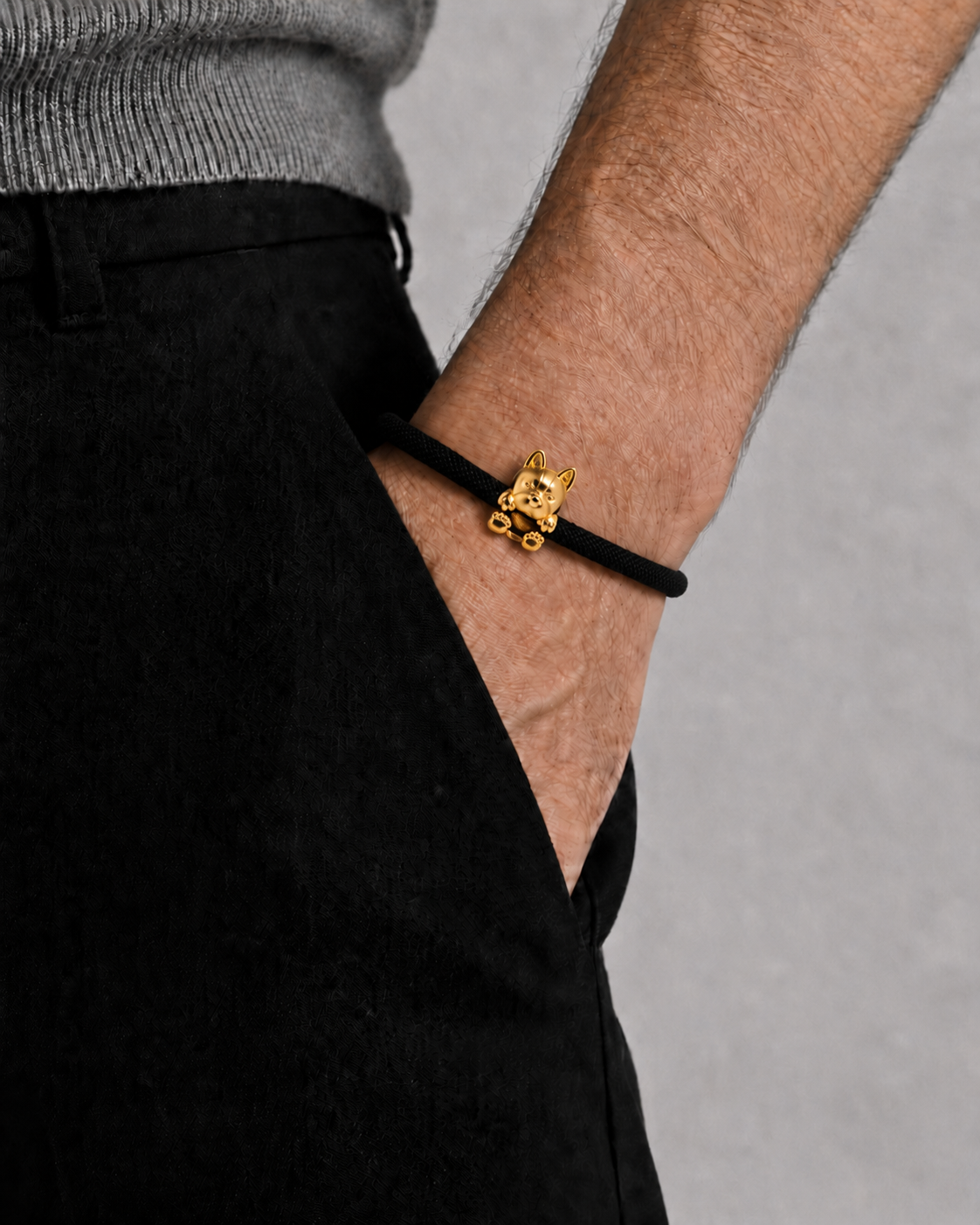 Person wearing a black bracelet with a gold cat charm on a gray background