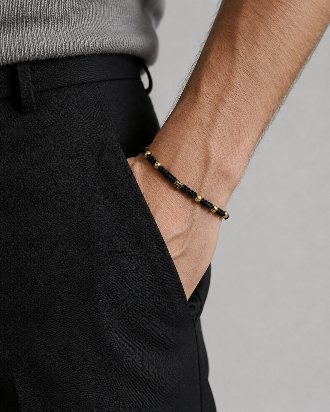 Person wearing a black and gold bracelet on a plain background