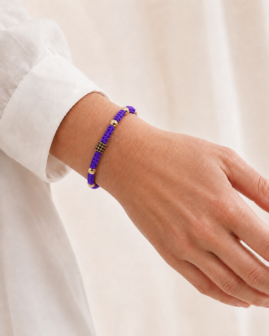 Hand wearing a purple beaded bracelet on a light background