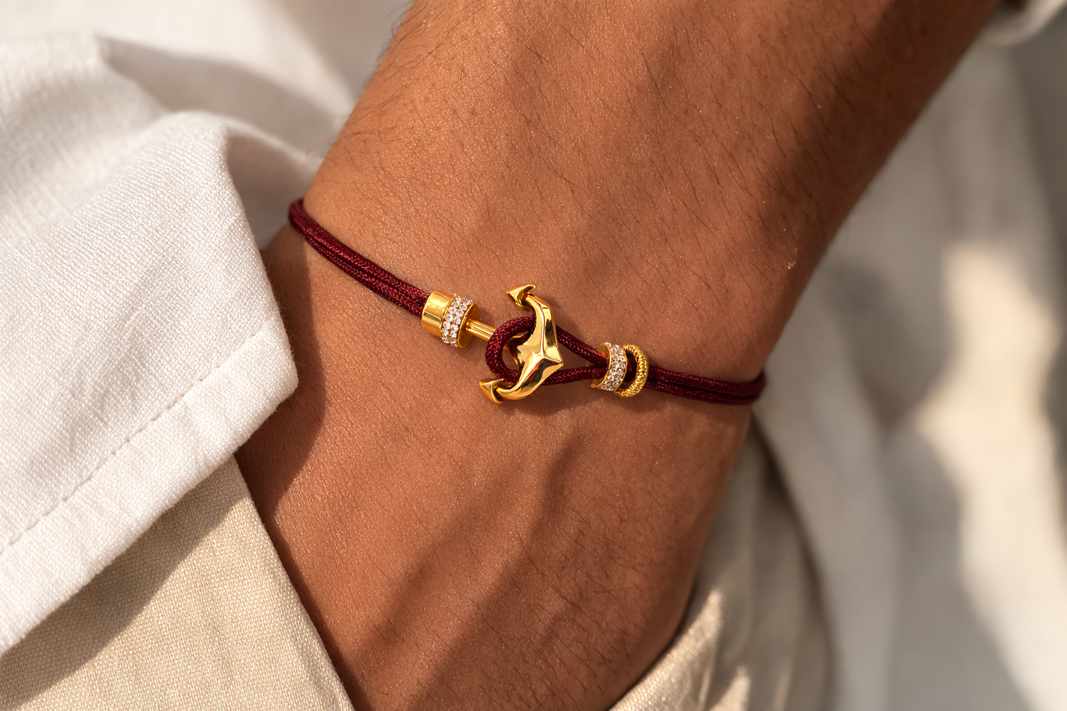 Bracelet with a gold anchor charm on a wrist, wearing a white shirt.