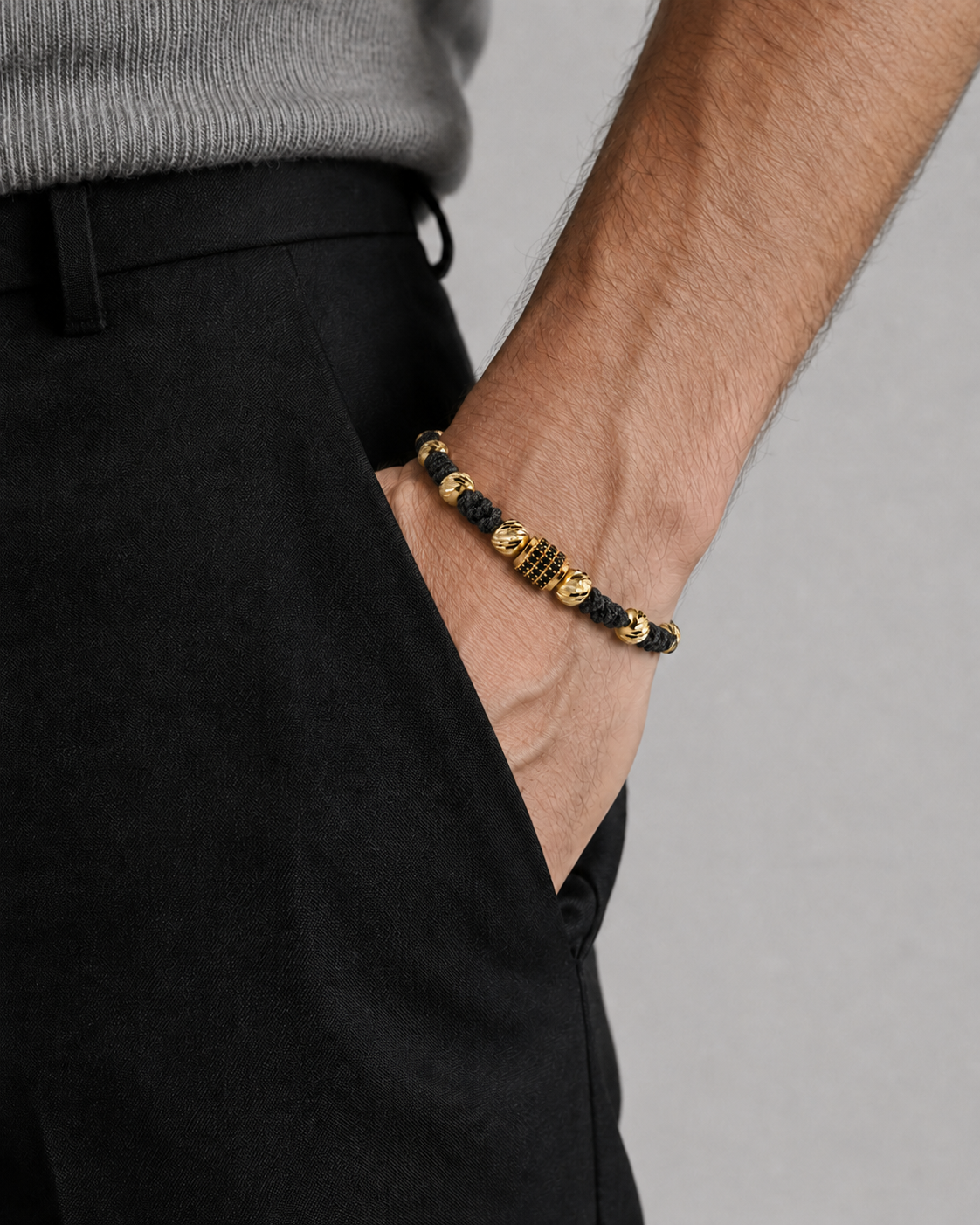 Person wearing a black and gold bracelet on a plain background